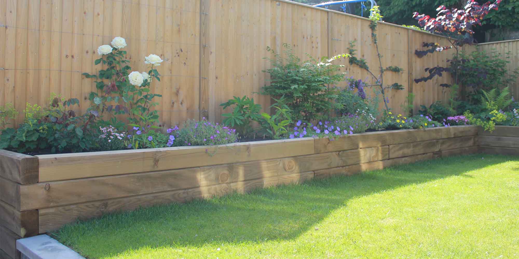Sleeper raised bed with flowering planting alongside a fence
