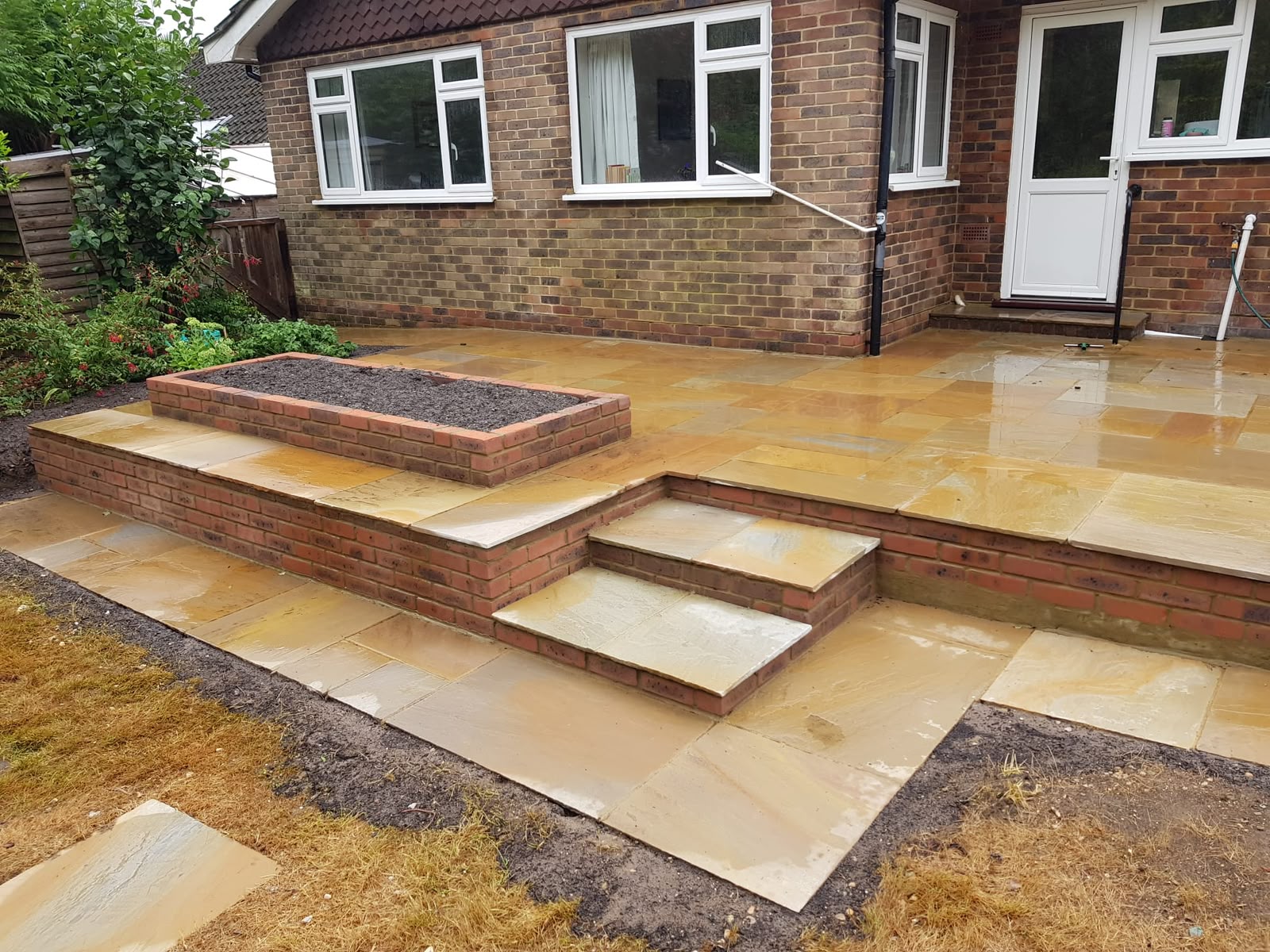 Raised sandstone patio and steps beside a brick house