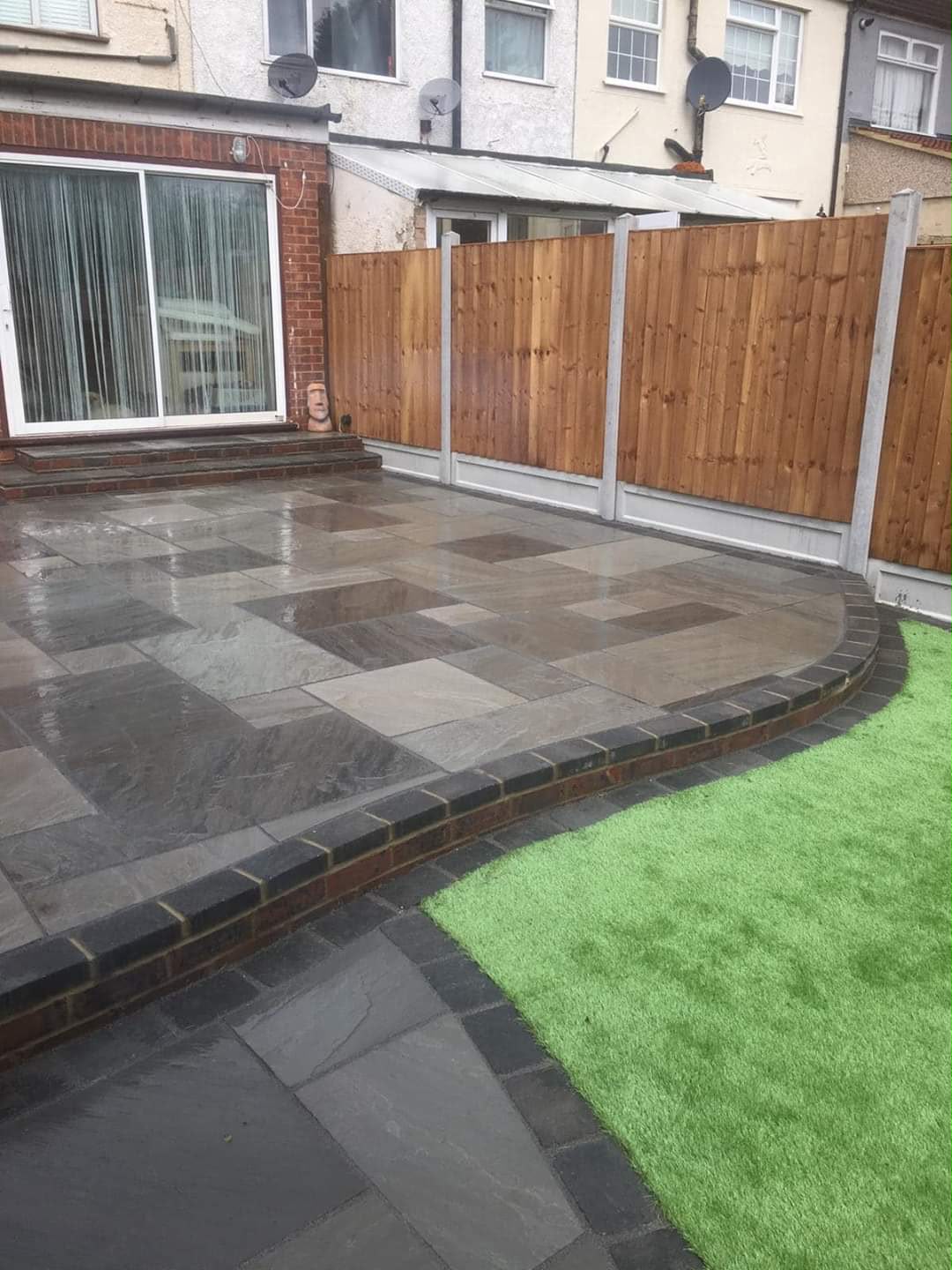 Dark stone patio with curved artificial-lawn edge
