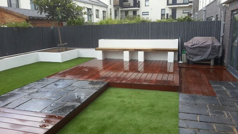 Artificial lawn behind decking with mature planting