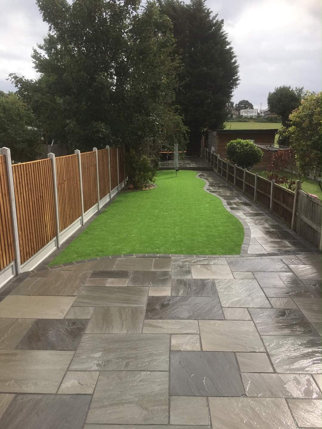 Dark stone path with striped lawn and timber fencing